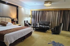 A hotel room with a large bed, a desk, two armchairs, a coffee table, and a chandelier. - Weihua Internationai Hotel (Hui'an)