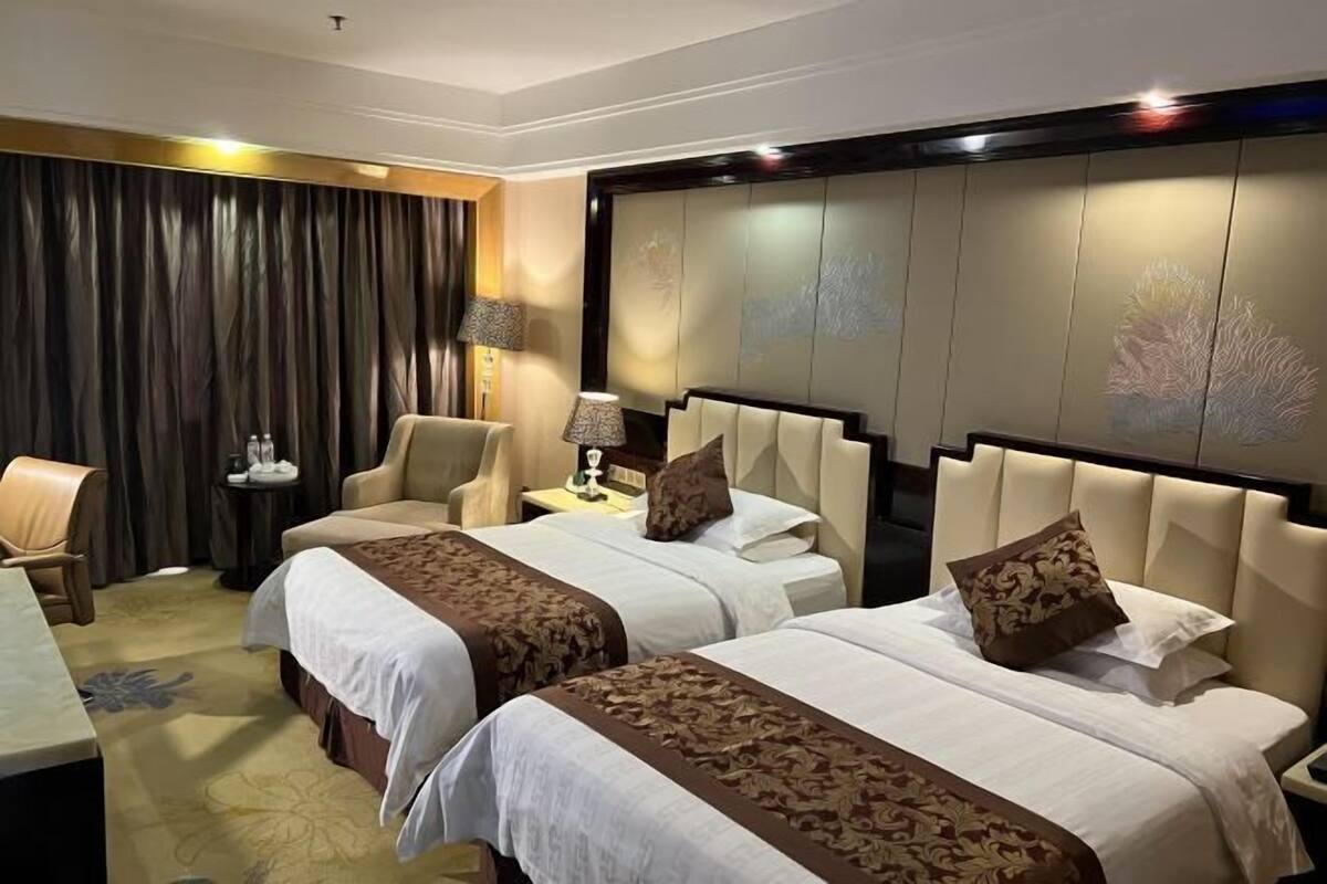 A hotel room with two beds, a sofa, a desk, and a lamp.