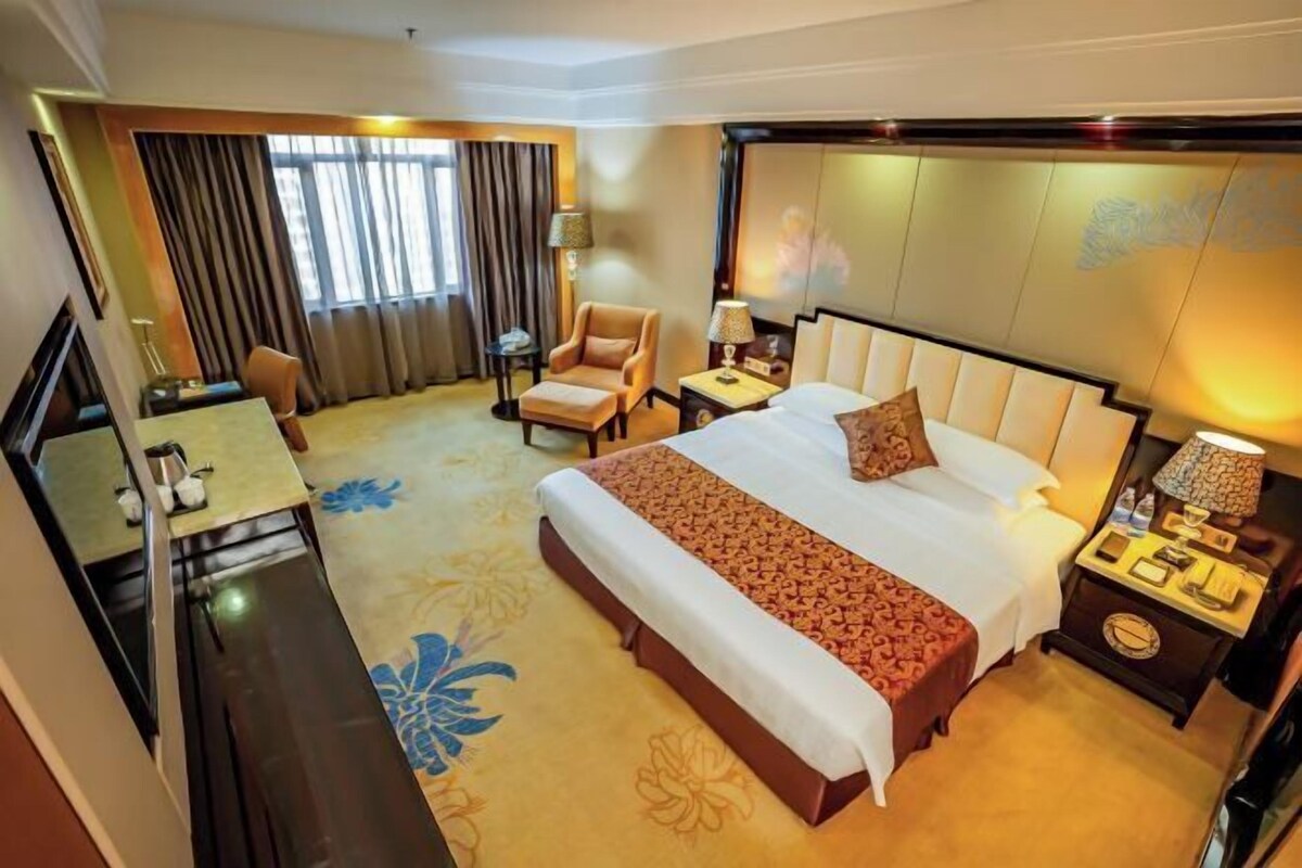 A hotel room with a large bed, a desk, a chair, a nightstand, and a TV.