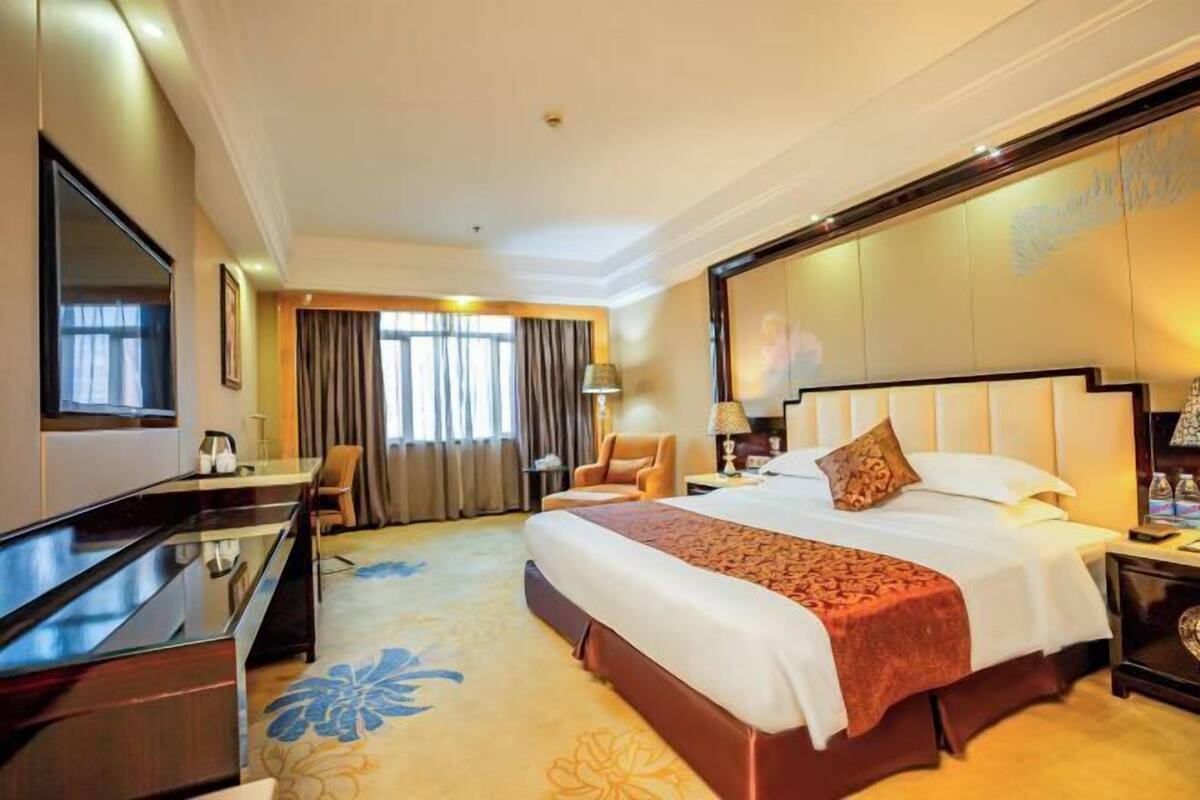 A hotel room with a large bed, a desk, a chair, and a TV.