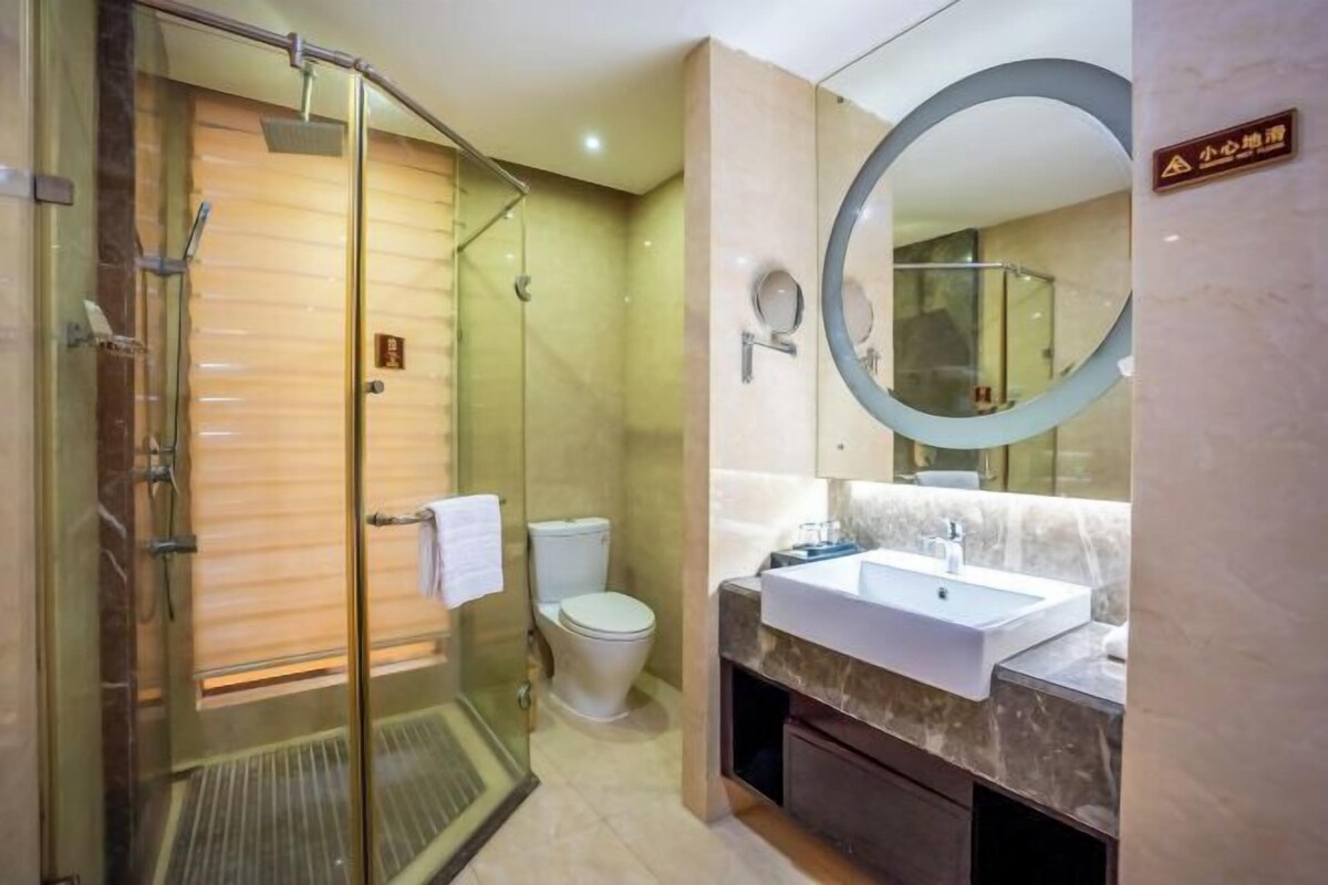 A modern bathroom with a glass-enclosed shower, a toilet, and a sink with a marble countertop.