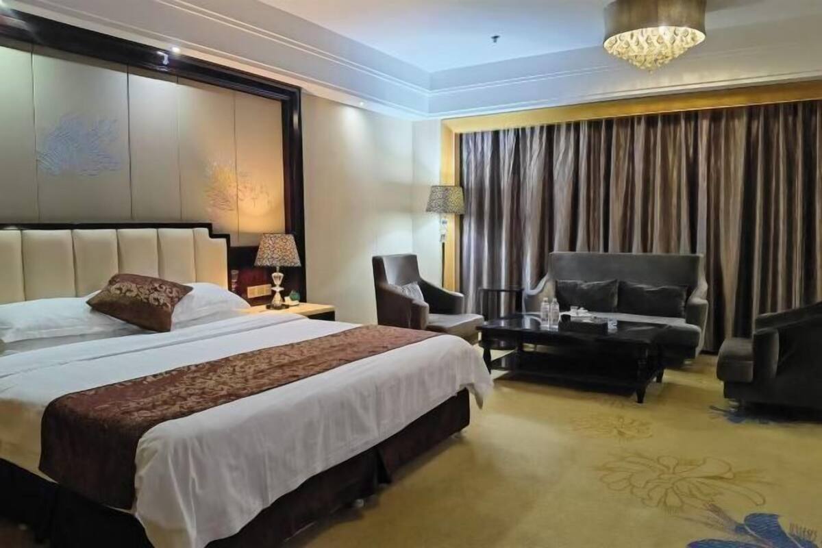 Una habitación de hotel con una cama grande, un escritorio, dos sillones, un sofá y una araña.