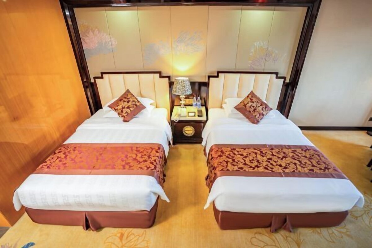 A hotel room with two beds, a nightstand with a lamp, and a decorative headboard.