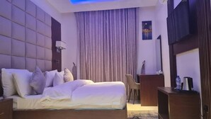 A modern hotel room with a large bed, a desk, a chair, and a TV. - Debbie's Suites and Apartments  (Orozo)