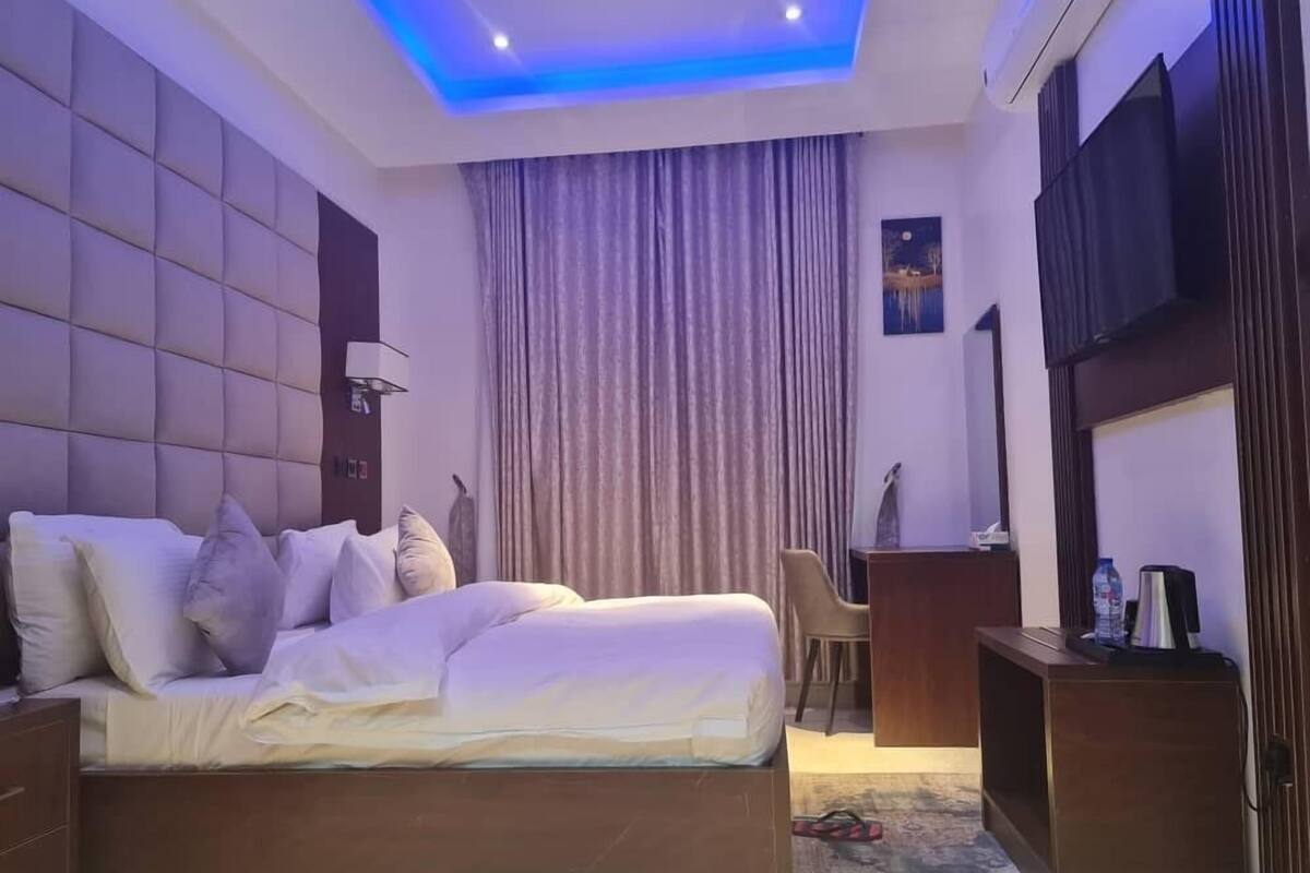 A modern hotel room with a large bed, a desk, a chair, and a TV.