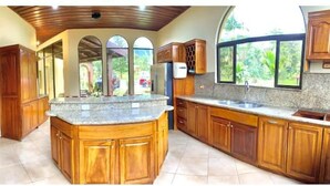 Una cocina amplia con armarios de madera, una isla de encimera de granito y ventanas grandes con vistas a un jardín.