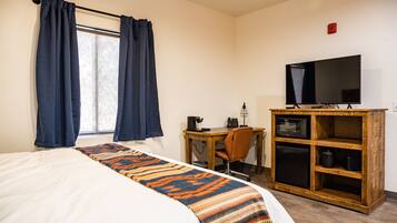 A hotel room with a bed, a desk with a computer, a television, and a wooden cabinet with kitchen appliances.
