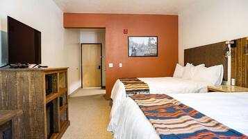 A hotel room with two beds, a television, a wooden desk, and a framed picture on the wall.