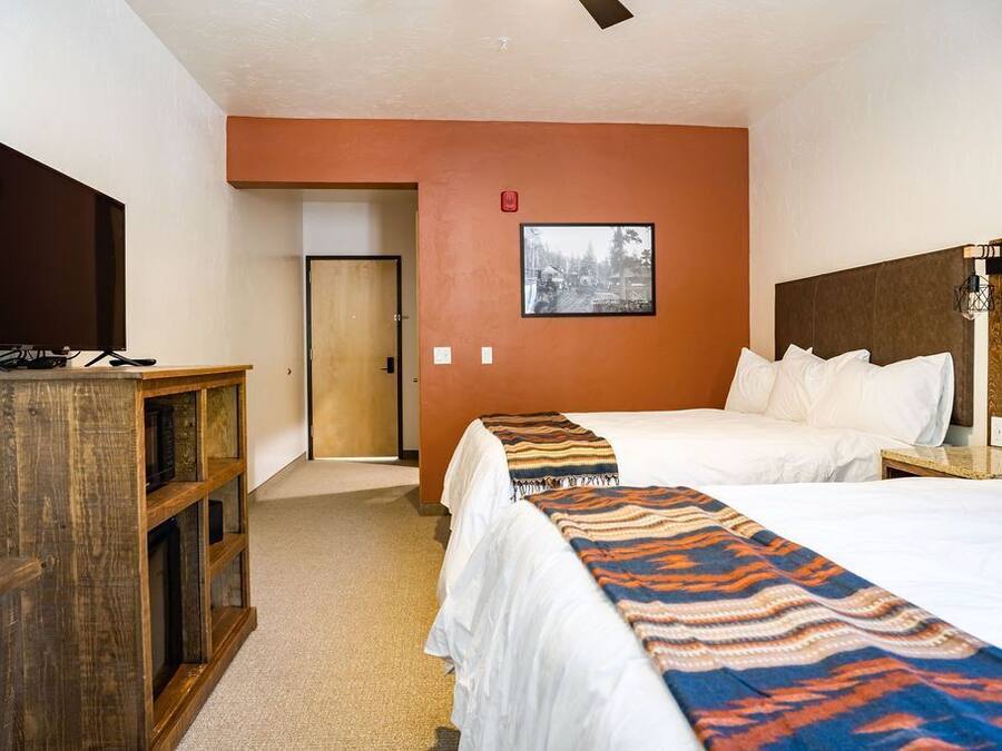A hotel room with two beds, a television, a wooden desk, and a framed picture on the wall.