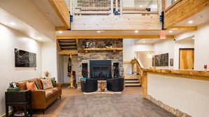 A spacious living area with a stone fireplace, wooden beams, and a high ceiling. - Grand Cloudcroft Hotel (Cloudcroft)