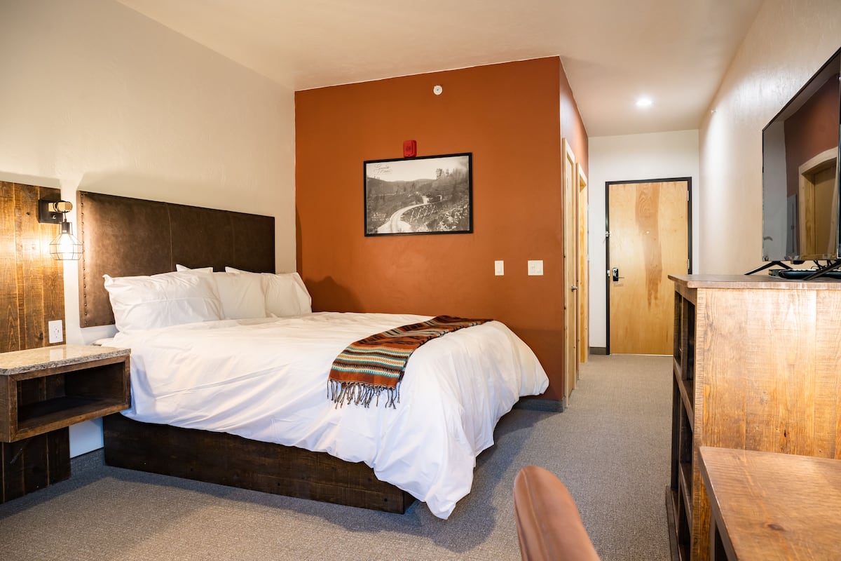 A bedroom with a wooden bed, a nightstand, a bedside table, a wooden desk, and a framed picture on the wall.