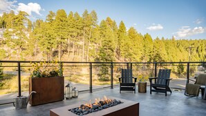 A rooftop terrace with a fire pit, outdoor seating, and a view of a forested area. - Grand Cloudcroft Hotel (Cloudcroft)