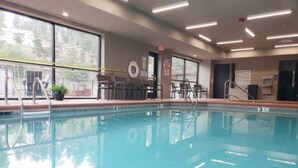 A clear indoor swimming pool with a lifeguard chair, pool ladder, and a view of the outside through large windows. - Grand Cloudcroft Hotel (Cloudcroft)