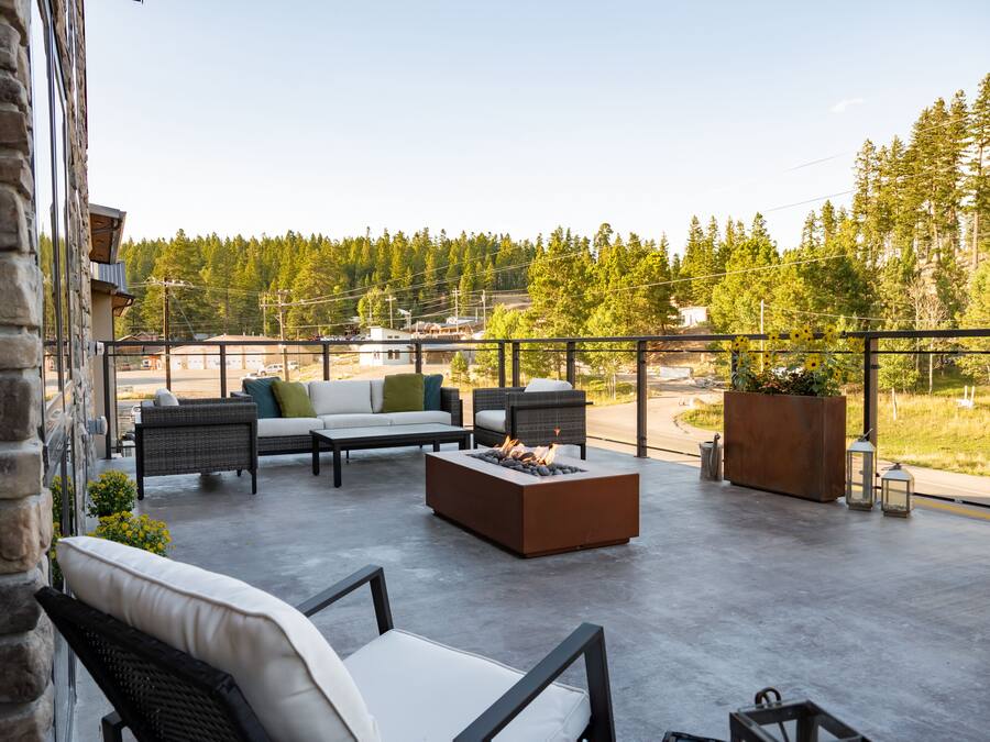 A spacious outdoor patio with a fire pit, seating area, and a view of a forested area.