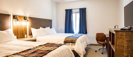 A hotel room with two beds, a desk, a chair, and a TV.