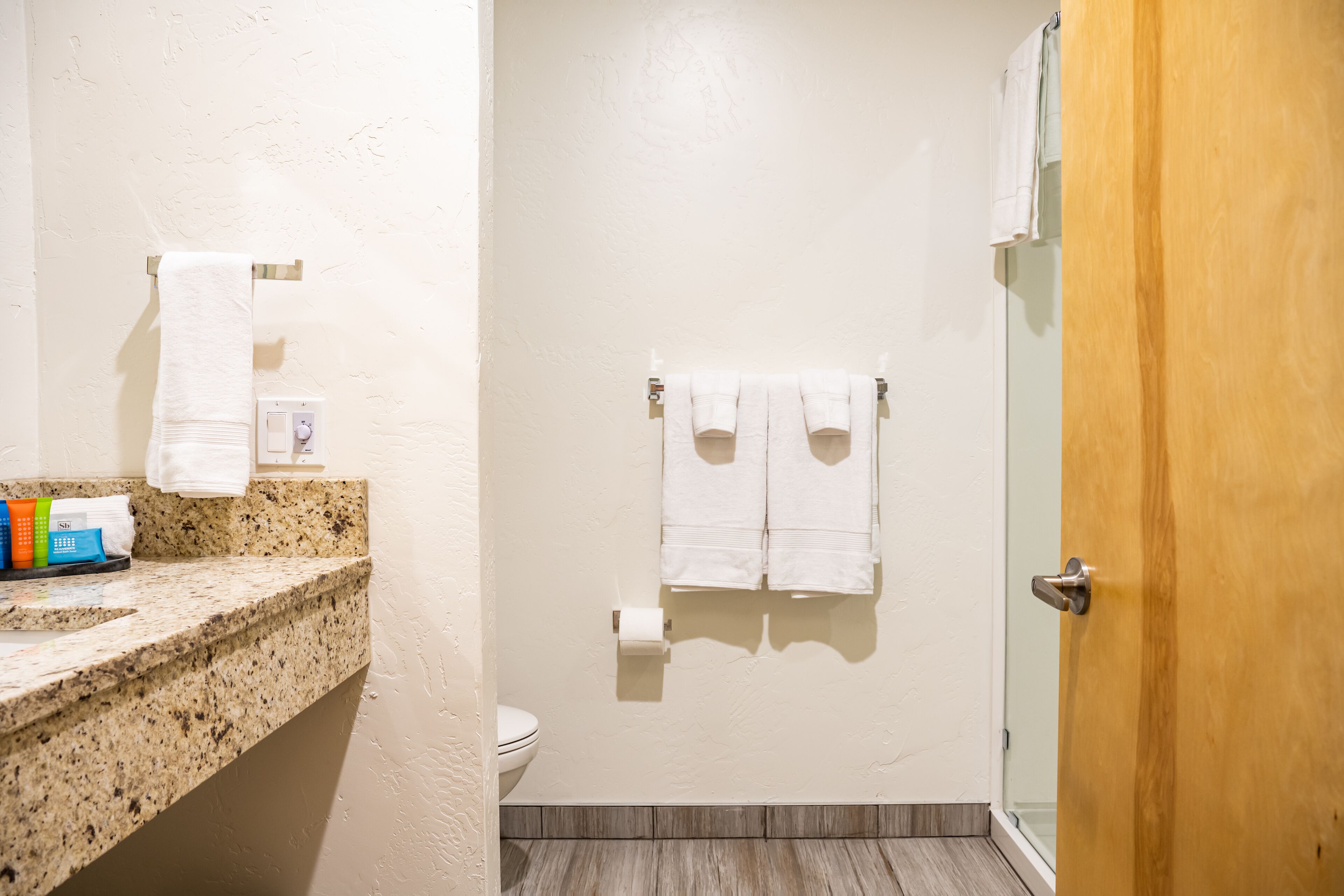 A bathroom with a granite countertop, a toilet, a towel rack with two towels, and a wooden door.