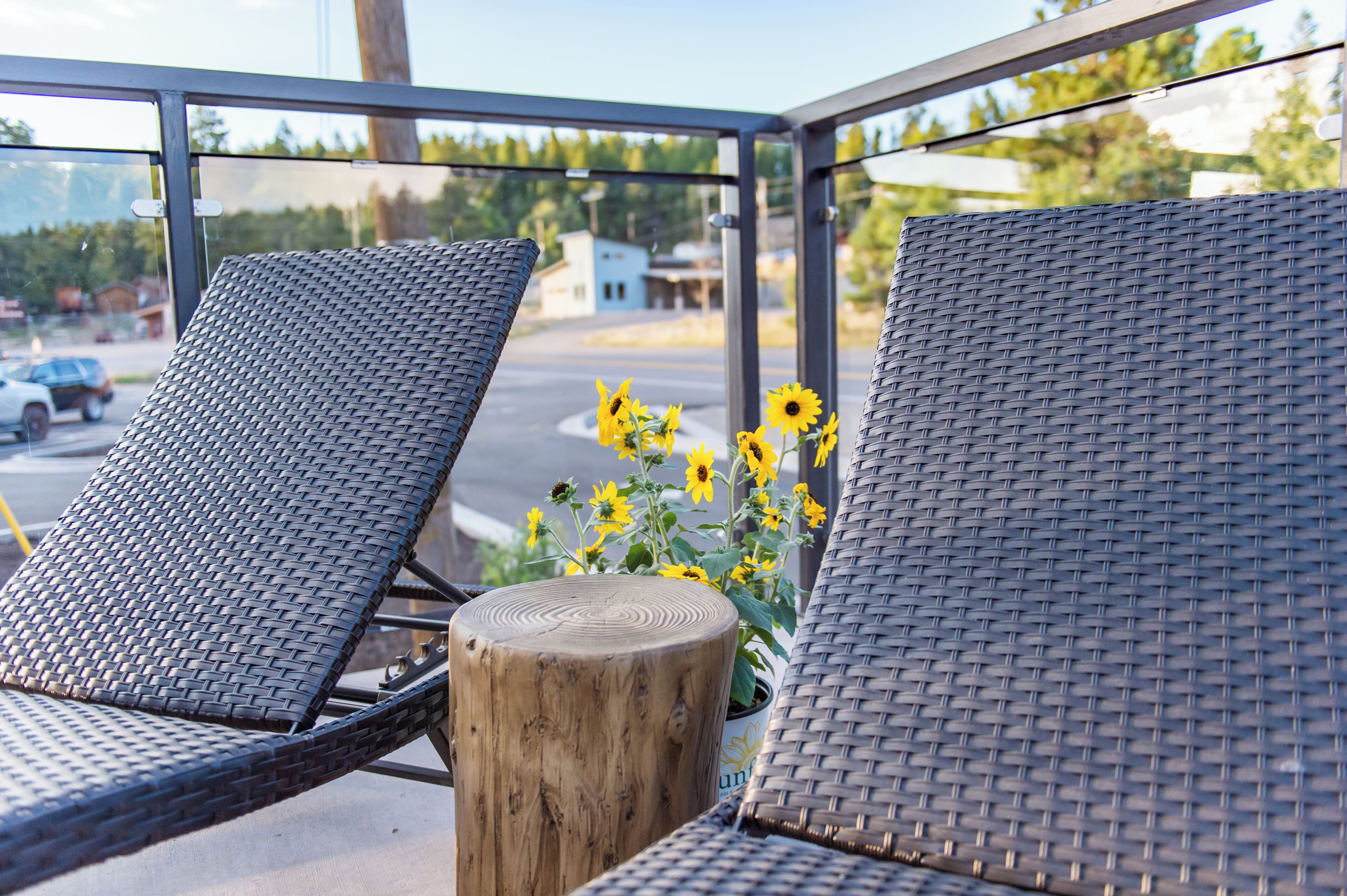 Two wicker lounge chairs with a wooden post and a potted plant with yellow flowers.