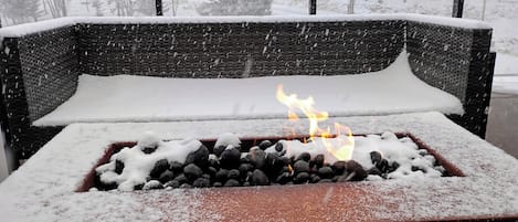 Ein mit Schnee bedeckter Außenbereich mit Sitzgelegenheiten und einem Feuerkorb in der Mitte.