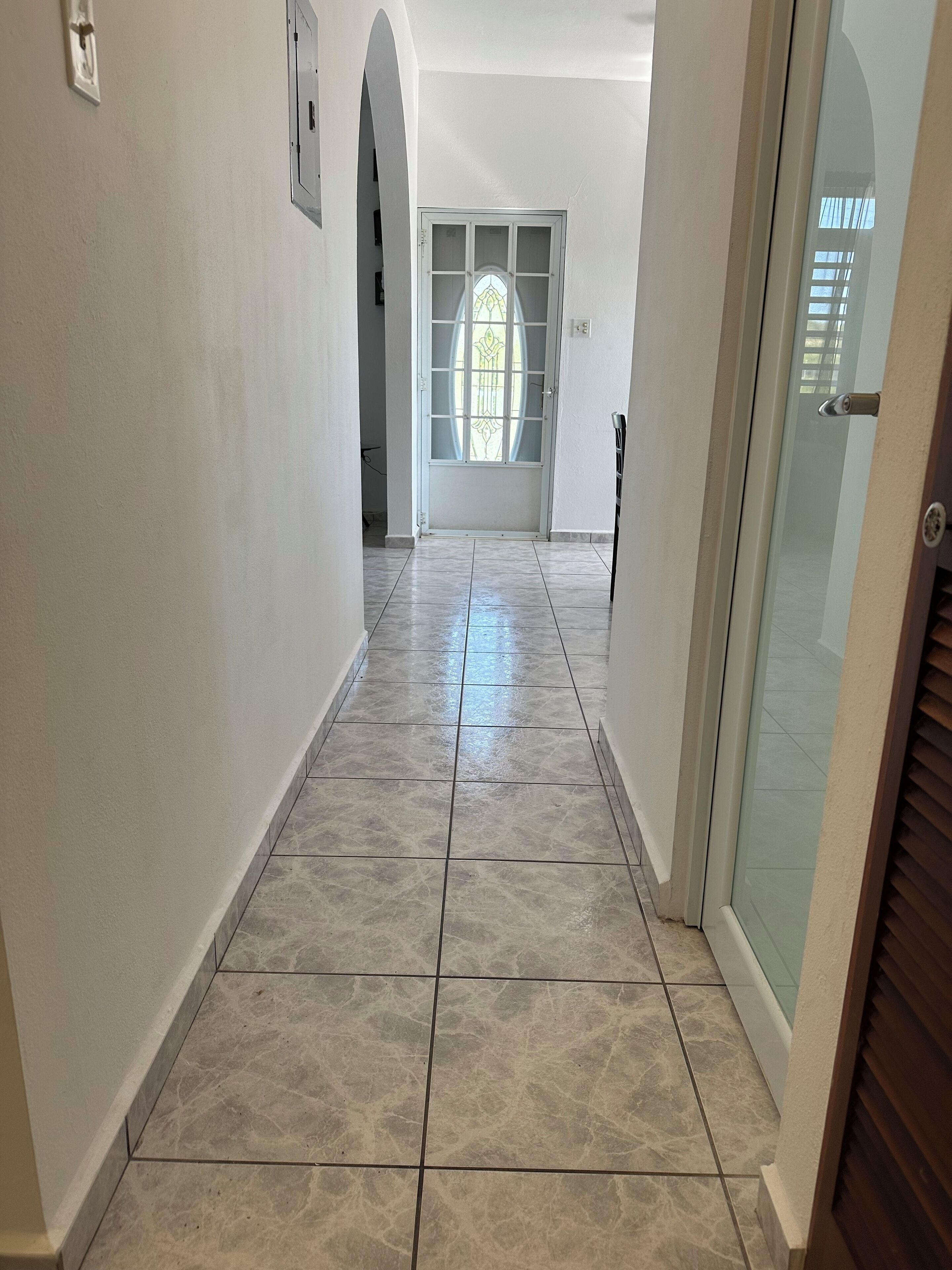 A hallway with tiled flooring, a glass door with a frosted glass panel, and a white wall with a small picture frame.