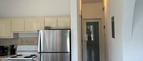 A modern kitchen with stainless steel appliances, a dining area with a table and chairs, and a hallway leading to a door.