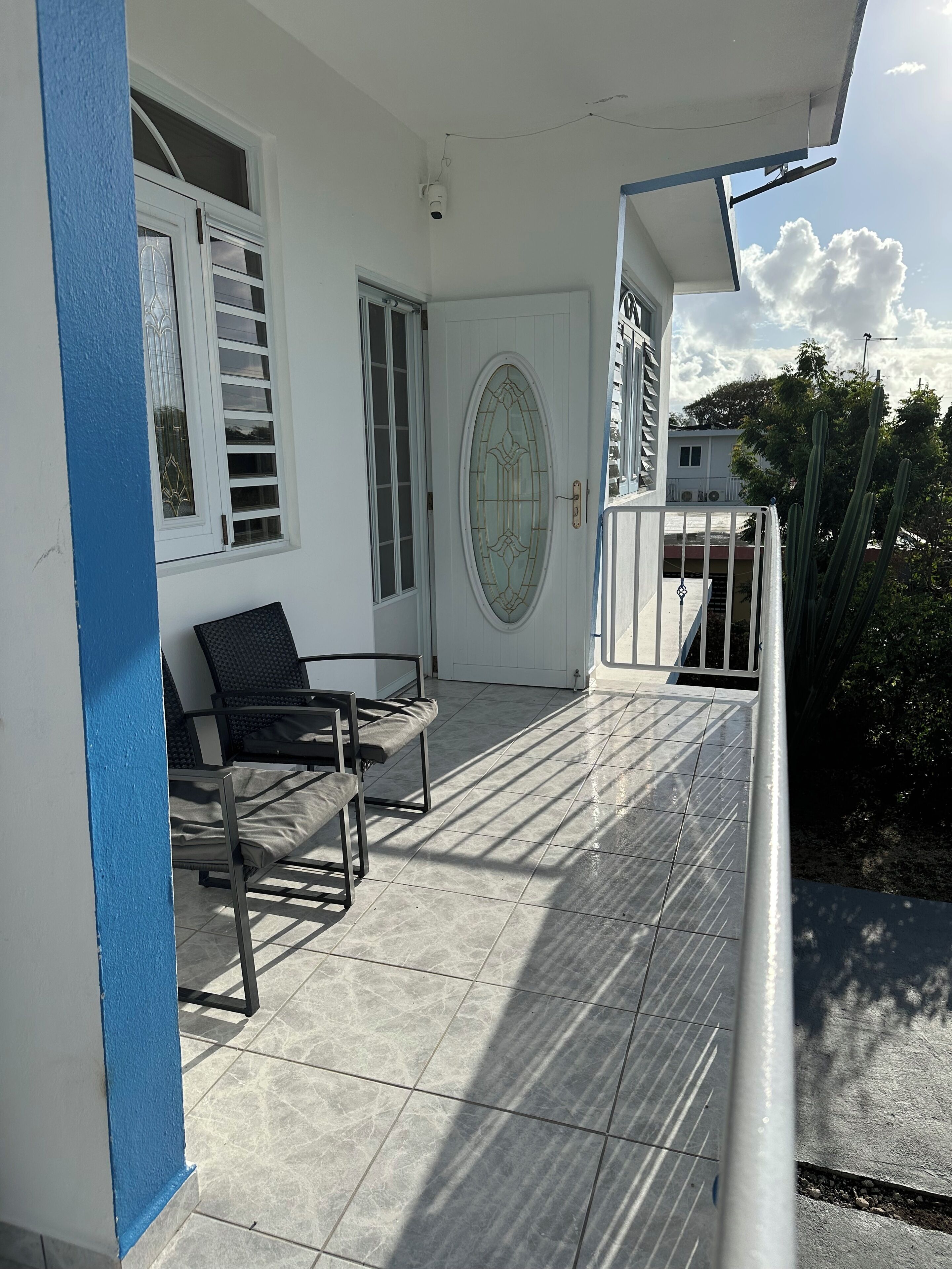 Un balcon doté d’un sol carrelé, d’une porte blanche avec un panneau de verre et d’un mur bleu.