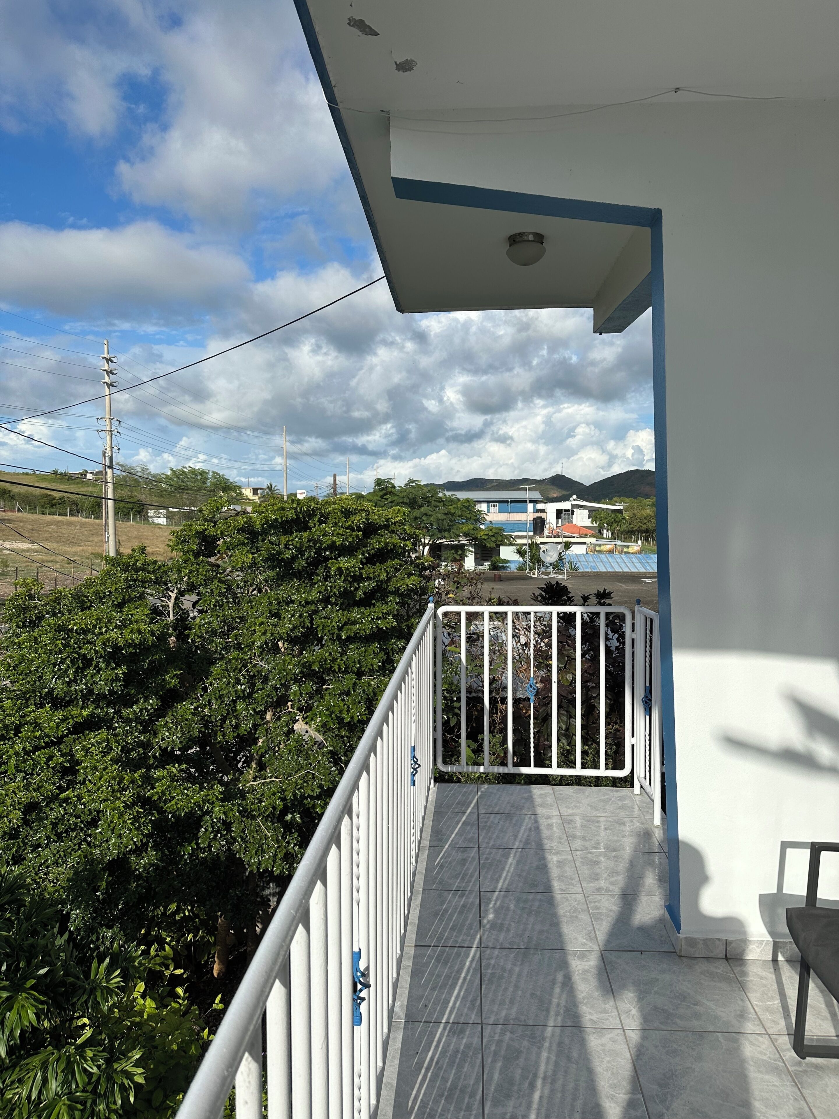 Un balcon donnant sur un immeuble, des arbres et un ciel nuageux.