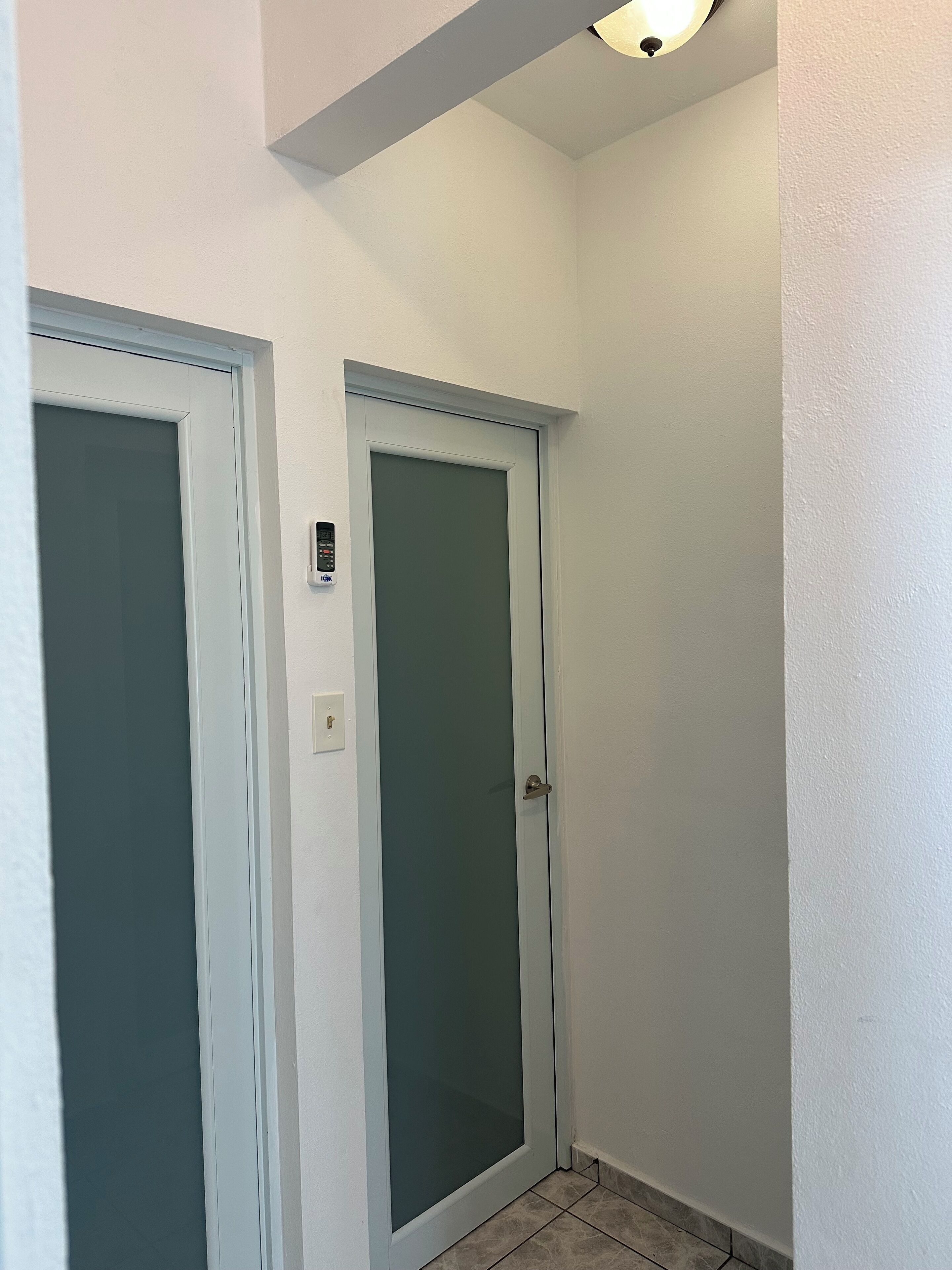 Un couloir avec deux portes : l’une est dotée d’un panneau en verre dépoli et d’une sonnette, et l’autre, d’un simple panneau en verre.
