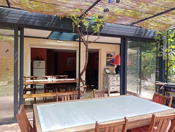 A dining area with a table and chairs, a glass partition, and a view of the interior. - Havre de paix swimming pool & pétanque - Gîte 3* 6 pers - Var (Pignans)