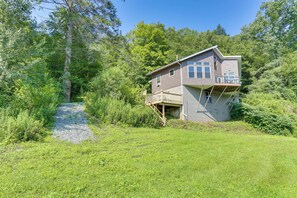 Ein zweistöckiges Haus mit Terrasse, umgeben von dichtem Grün und Bäumen.