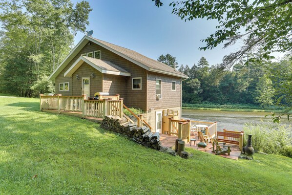 Eine Hütte mit einer Terrasse, Sitzgelegenheiten im Freien und Blick auf einen Fluss.