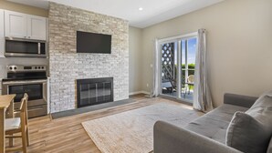A modern kitchen with a stone wall, built-in microwave, oven, and a flat-screen TV. - Atlantic Bluffs Club (Montauk)