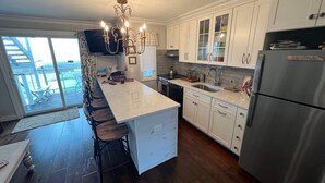 A modern kitchen with white cabinets, a stainless steel refrigerator, and a large island with bar stools. - Atlantic Bluffs Club (Montauk)
