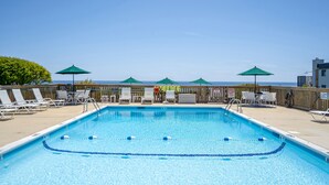 A swimming pool with clear blue water, surrounded by lounge chairs and umbrellas, with a view of the ocean in the background. - Atlantic Bluffs Club (Montauk)