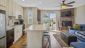 A modern kitchen with white cabinets, a central island, and a dining area with a blue sofa and green cushions. - Atlantic Bluffs Club (Montauk)