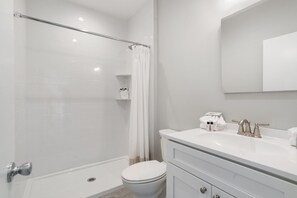 A modern bathroom with a glass shower enclosure, a white toilet, and a vanity with a mirror. - Atlantic Bluffs Club (Montauk)