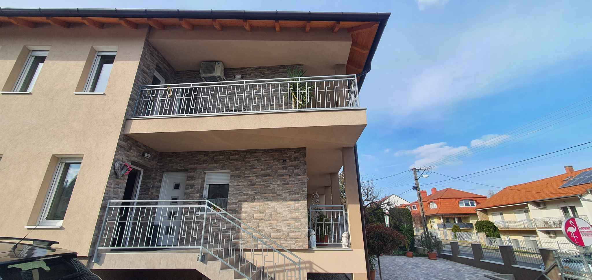 A two-story building with a stone facade, a balcony with metal railings, and a door with a small window.