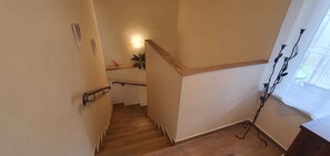 Un escalier avec des marches en bois et une rampe, menant à un palier agrémenté d’une plante et d’un luminaire fixé au mur.