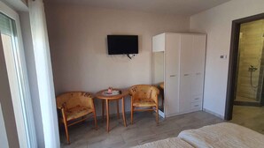 Ein Hotelzimmer mit einem Bett, zwei Sesseln, einem kleinen Tisch, einem Kleiderschrank und einem an der Wand befestigten Fernseher.