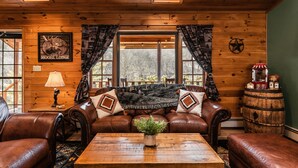 Interior acogedor de una cabaña con muebles de cuero, una mesa de madera y un ventanal con cortinas.