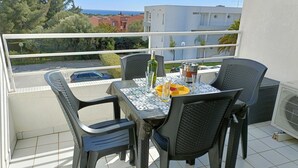 Ein Balkon mit Tisch und Stühlen, einer Flasche, Gläsern und einem gelben Teller.