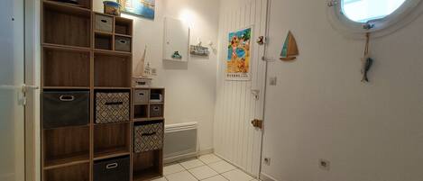A hallway with a white door, a small window, and a shelf unit with storage bins.