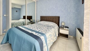 A bedroom with a large bed, a nightstand, a mirror, and a radiator. - Bright and quiet apartment near the sea (Saint-Raphaël)