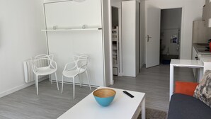 Un salon moderne avec un canapé blanc, une table basse blanche surmontée d’un bol bleu, deux chaises blanches et un meuble blanc avec des étagères.