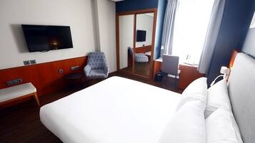 Habitación de hotel con una cama grande, un televisor montado en la pared, una silla, un escritorio y un espejo.