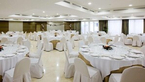 Un amplio salón de banquetes con varias mesas redondas dispuestas para cenar, cada una con mantel blanco y sillas a juego.