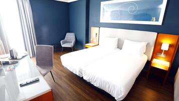 Habitación de hotel con una cama grande, un escritorio, una silla y una obra de arte colgada en la pared.