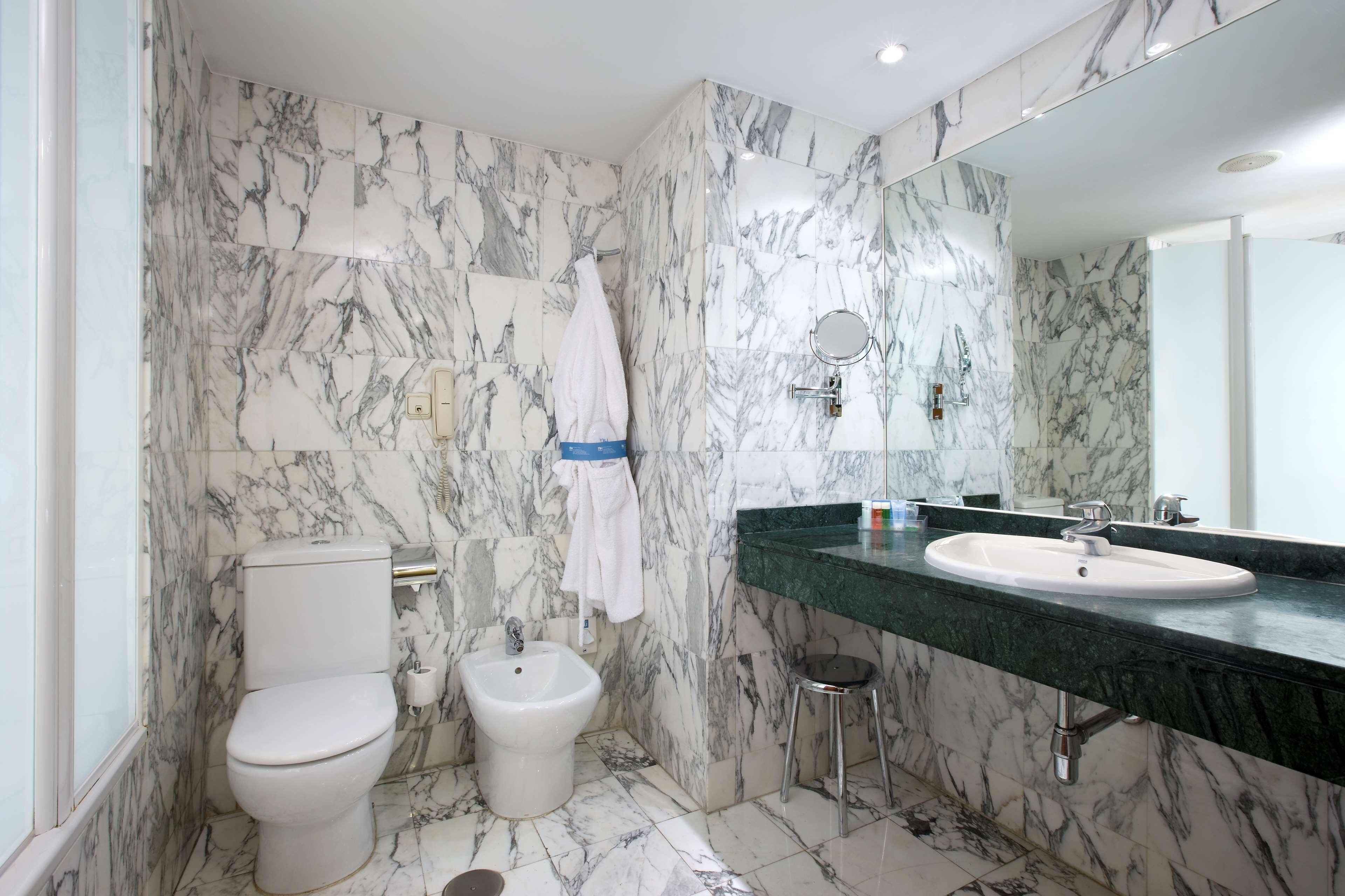 Ein Badezimmer mit Toilette, Bidet und Waschbecken, alles vor Marmorwänden.
