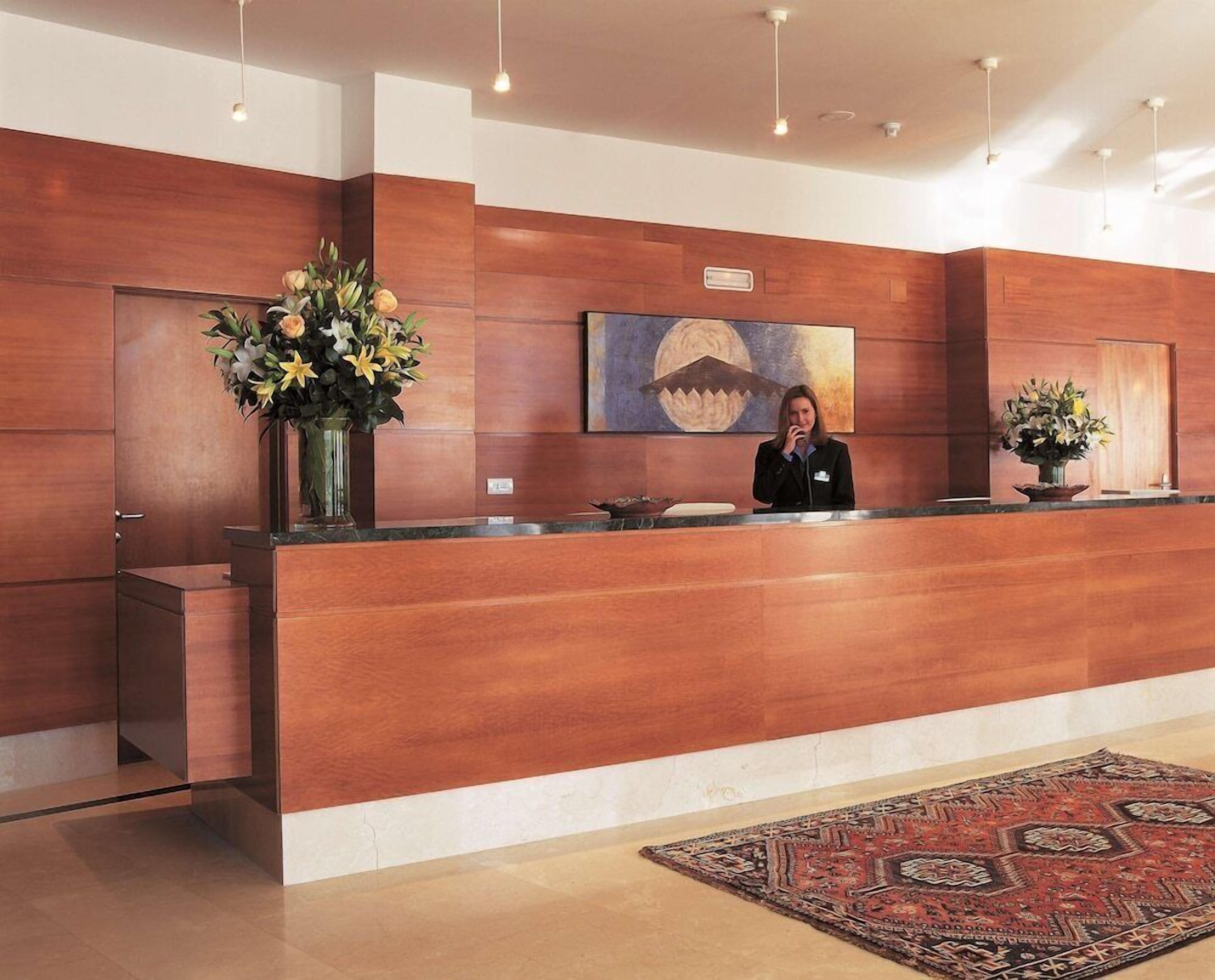 Un mostrador de recepción con una recepcionista, paneles de madera, un cuadro y una alfombra.