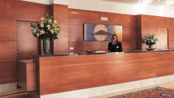 Un mostrador de recepción con una recepcionista, paneles de madera, un cuadro y una alfombra.
