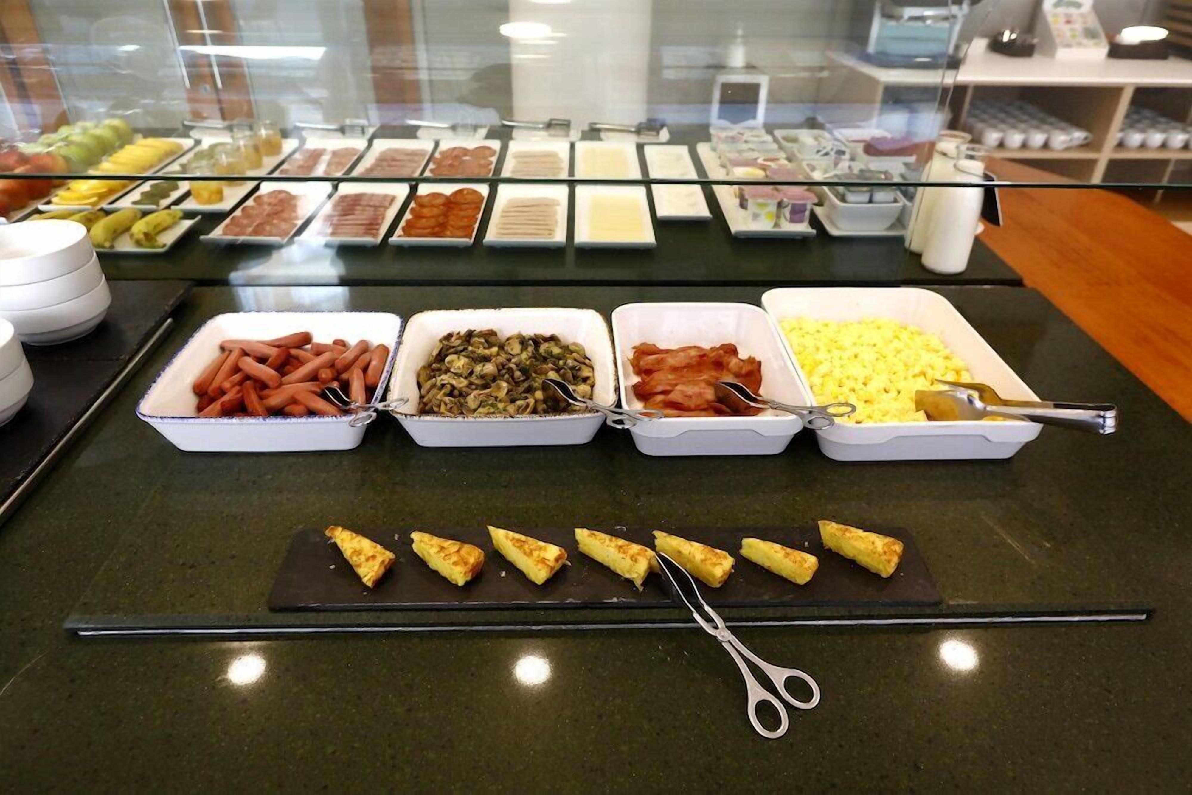 Un bufé con diversas opciones de comida, incluyendo perros calientes, champiñones, tocino y huevos revueltos.